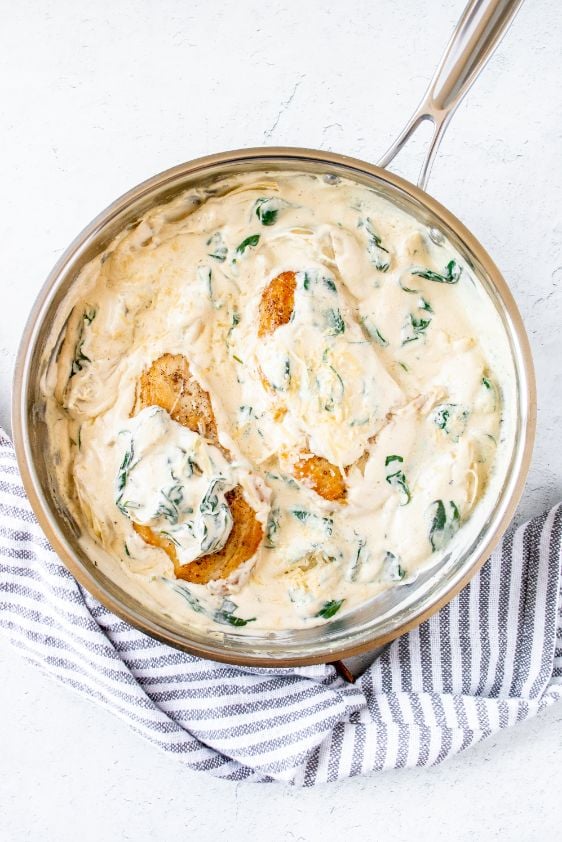 Chicken breasts added to a large skillet with a creamy spinach and artichoke sauce