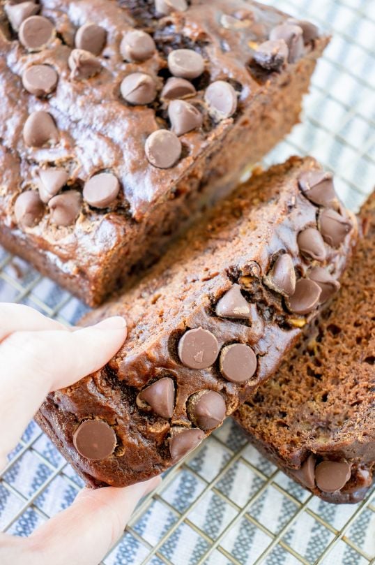 A hand reaching for a slice of chocolate chip bread which has been sliced and is cooling on a wire rack