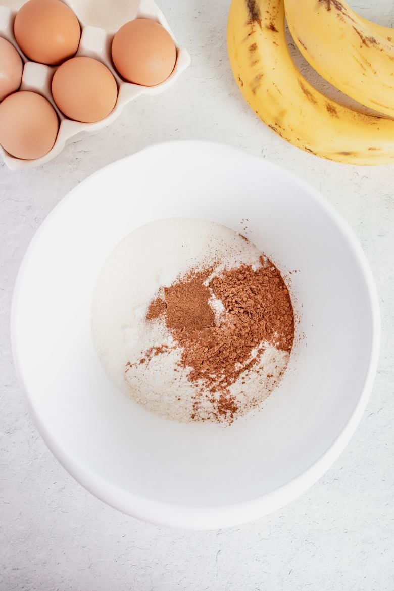 Overhead shot of dry ingredients for a banana bread added to a white bowl