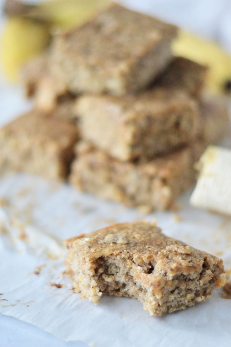 A stack of banana snack bars in the background with a half eaten bar in the foreground