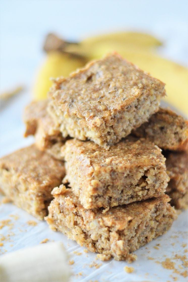A stack of banana bars one on top of the other with some ripe bananas in the background