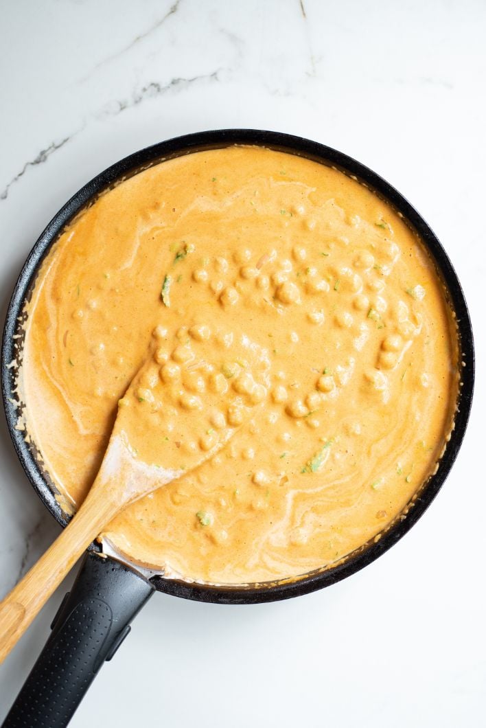 Chickpea curry being stirred with a wooden spoon in a black saucepan