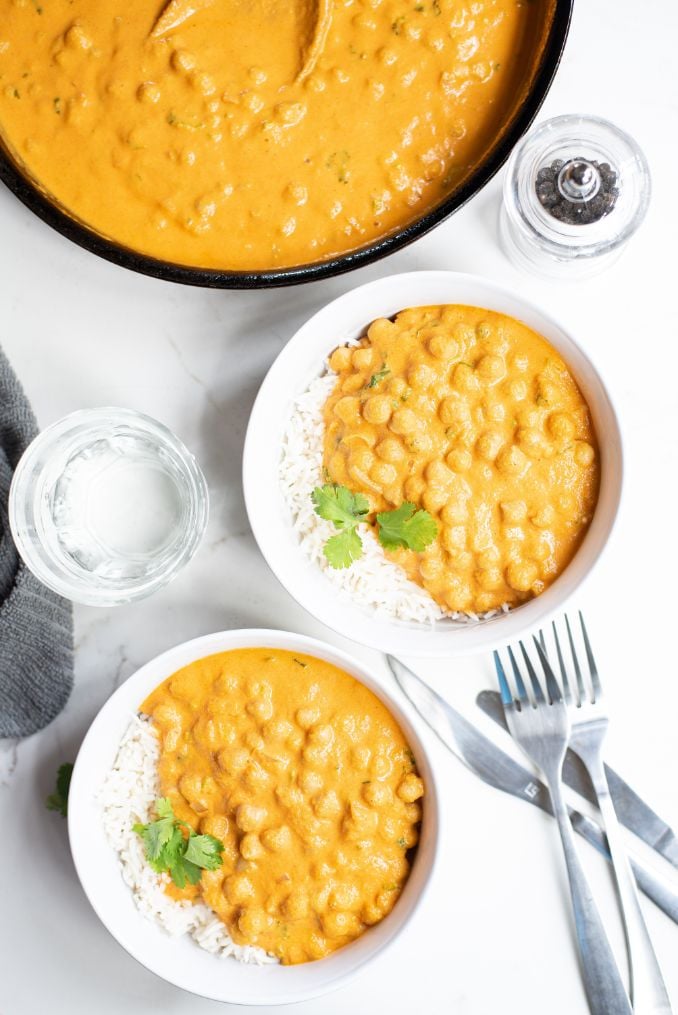 Chickpea curry served in white bowls with rice and topped with some chopped cilantro