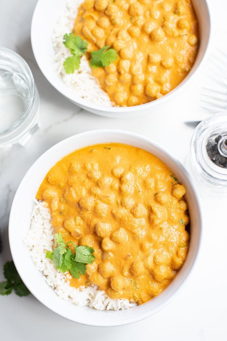 2 white bowls holding a creamy pumpkin and chickpea curry topped with fresh cilantro