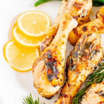 Grilled drumsticks served on a white platter along with lemon wedges, green beans and fresh rosemary