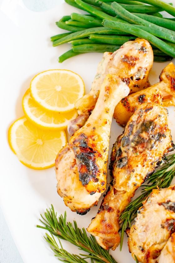 Grilled drumsticks served on a white platter along with lemon wedges, green beans and fresh rosemary