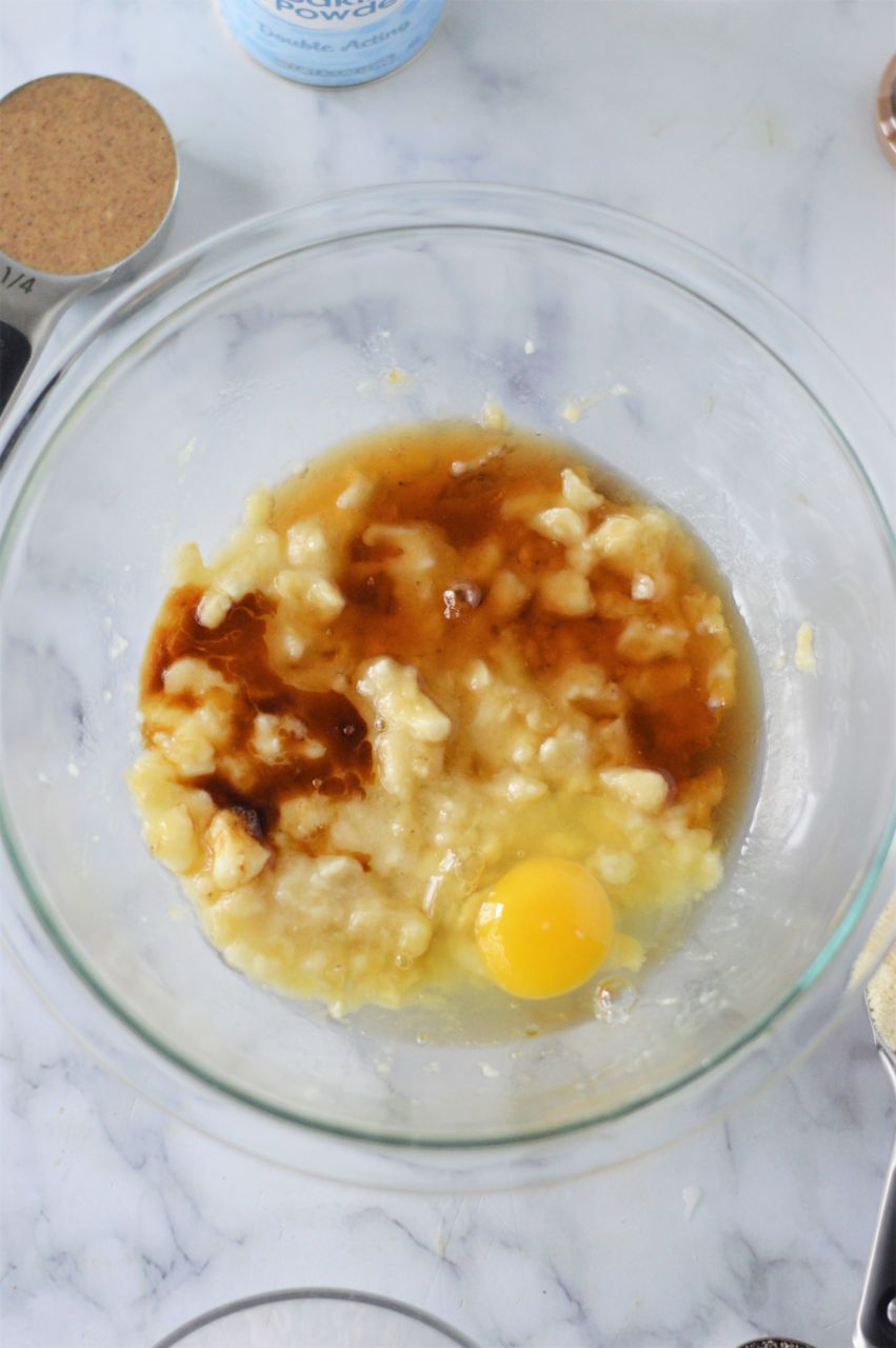 Eggs and maple syrup added to mashed banana in a glass bowl