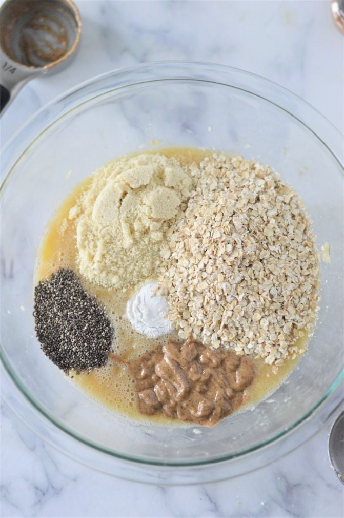Oats, almond flour, almond butter and chia seeds added to a banana mixture in a glass bowl