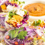 Chopped veggie summer rolls arranged on a platter with a peanut dipping sauce