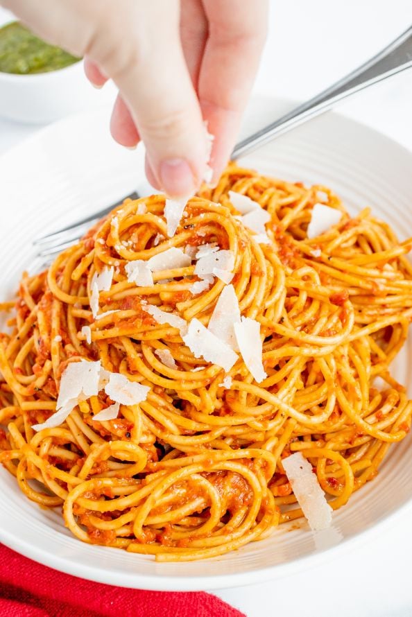 A hand sprinkling some parmesan on top of pesto pasta