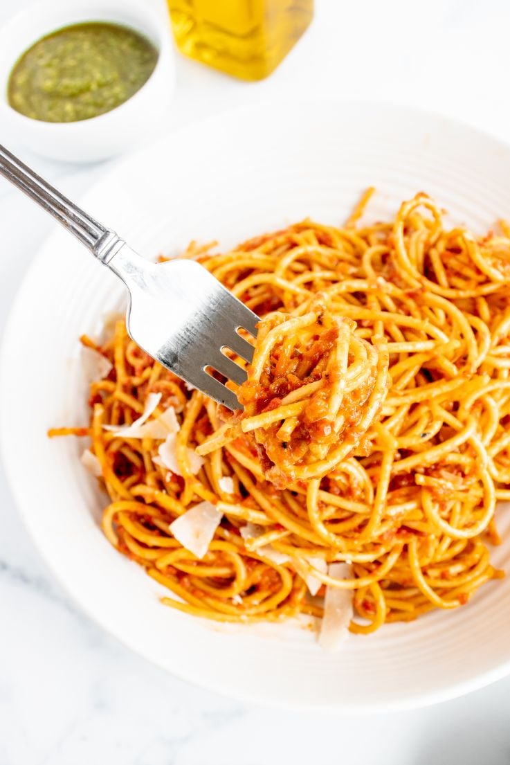 A fork picking up some spaghetti with a roasted red pepper pesto sauce