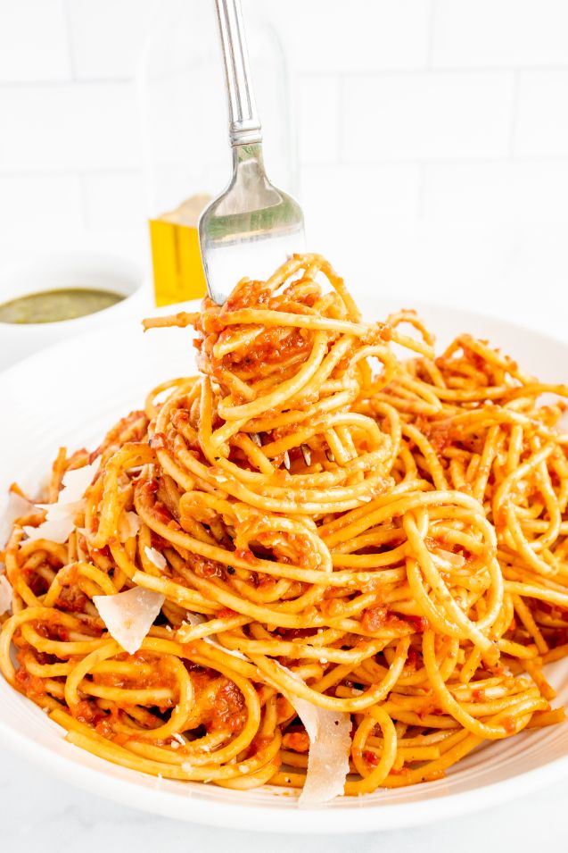 A fork swirling some pasta with red sauce served in a white bowl