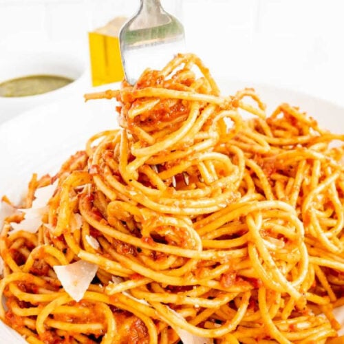 A fork picking up some spaghetti with a roasted red pepper pesto sauce