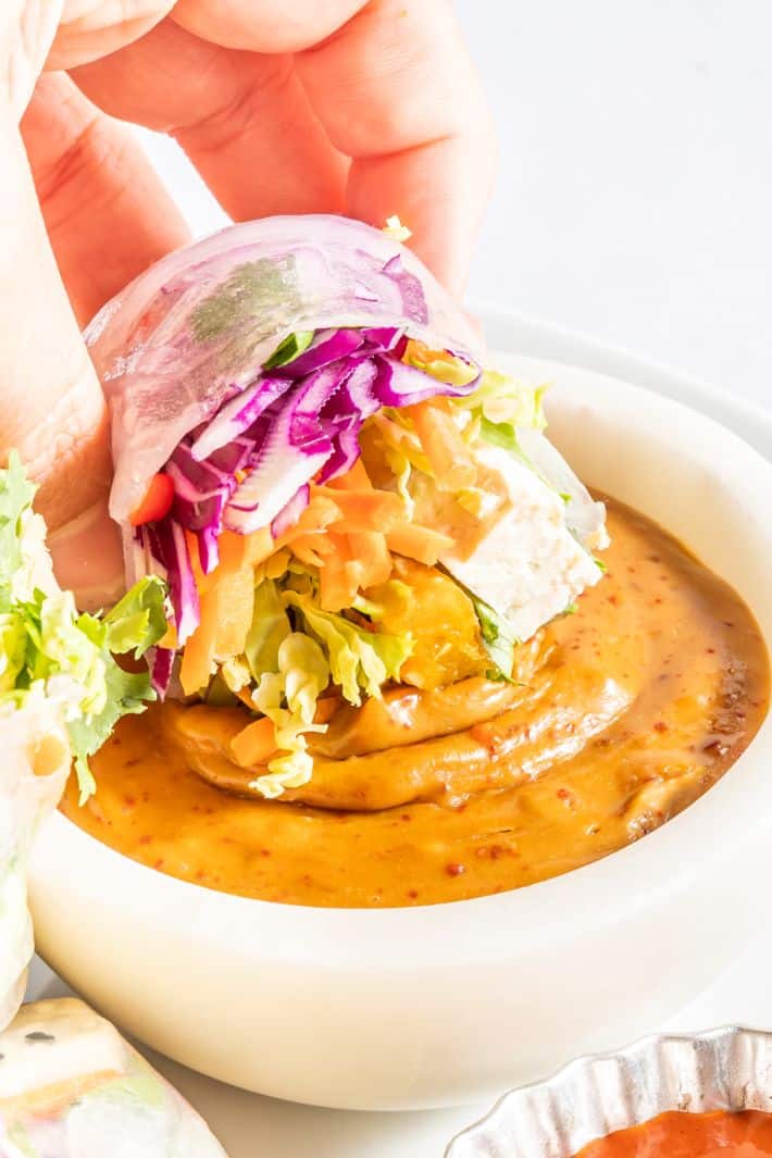 A vegan summer roll being dipped into a peanut dipping sauce