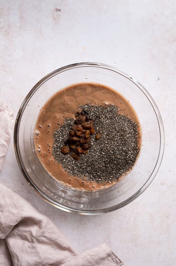 Dried fruit and chia seeds added to a liquid chocolate mixture in a large glass bowl