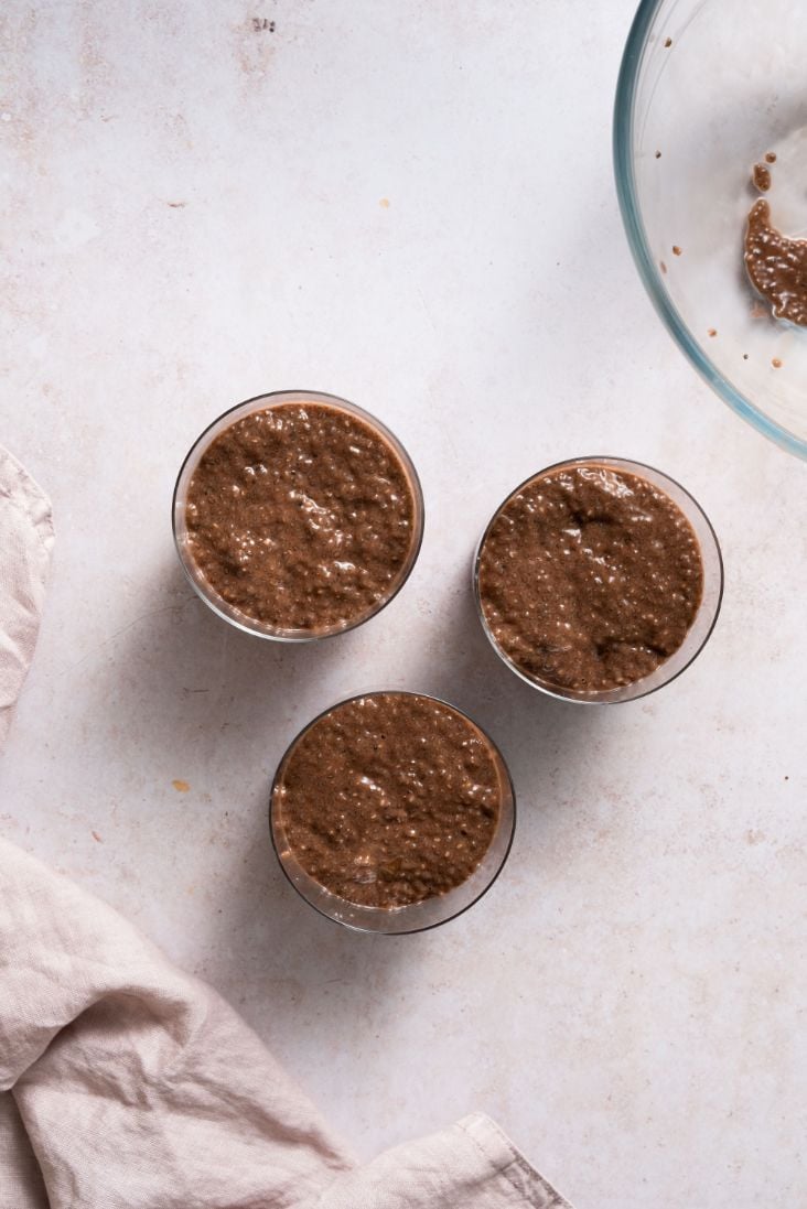 Chia pudding mixture being transferred from a large glass bowl into 3 smaller glass bowls