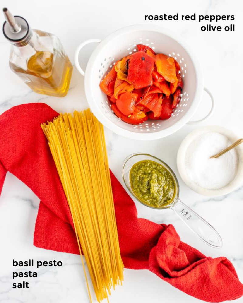 Overhead shot of all the ingredients required for making a pasta dish with roasted red peppers and pesto