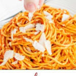 A fork picking up some spaghetti with a roasted red pepper pesto sauce