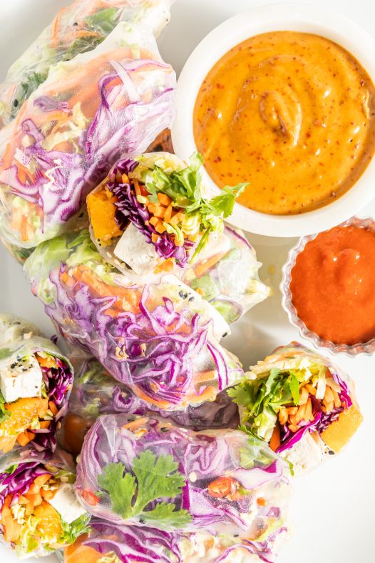 Overhead shot of summer rolls piled onto a white serving platter with dipping sauces on the side.