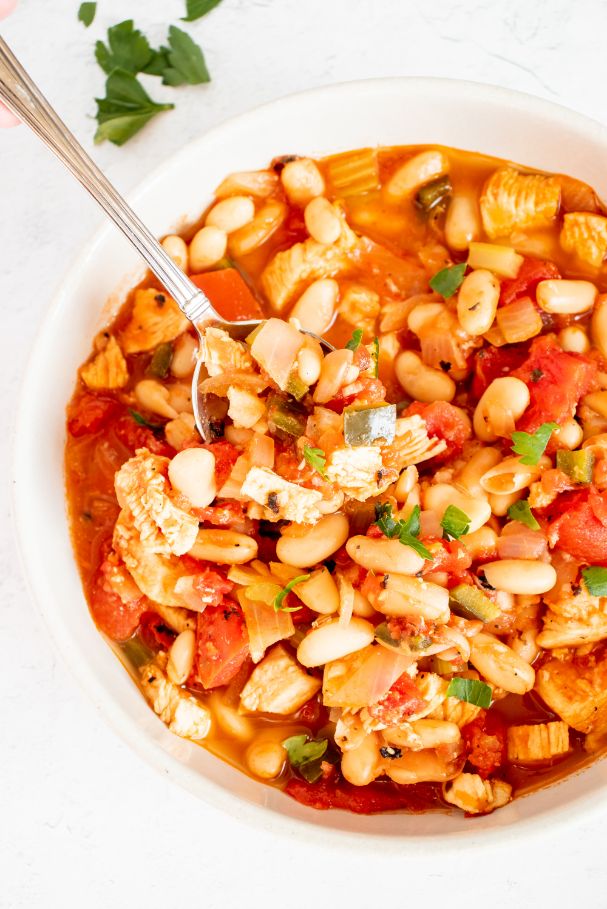 A thick bowl of bean stew being served with a silver spoon from a large white bowl