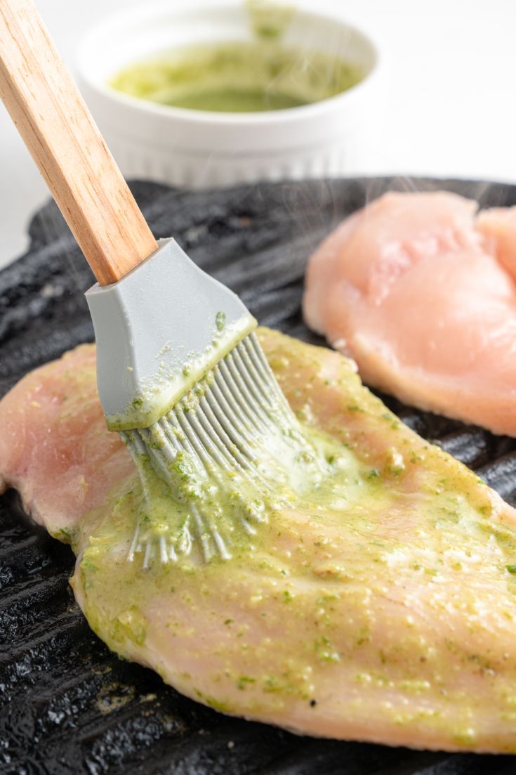 Basting a raw chicken breast on an indoor grill pan with extra pesto