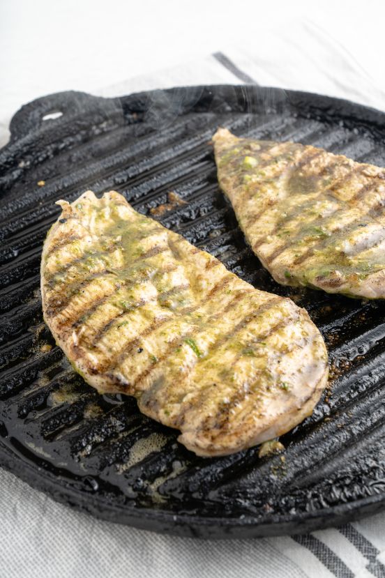 Two chicken breast halves on an indoor grill pan being cooked