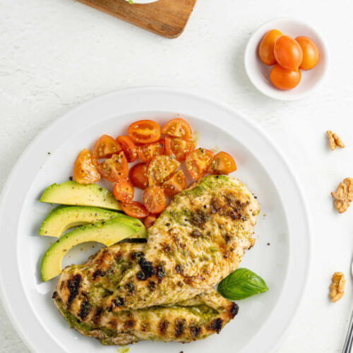 Grilled pesto chicken on a white plate with tomatoes and avocado
