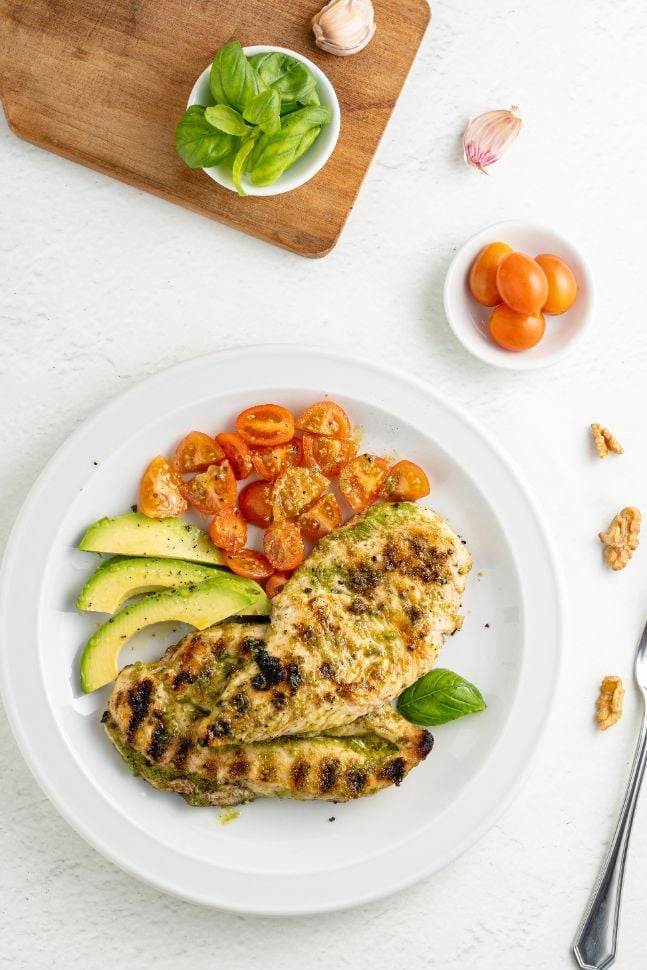 overhead shot of grilled chicken with a pesto marinade and sserved with tomatoes and avocado