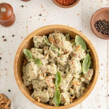 Up close shot of a wooden bowl containing potato salad with a creamy dressing and fresh basil