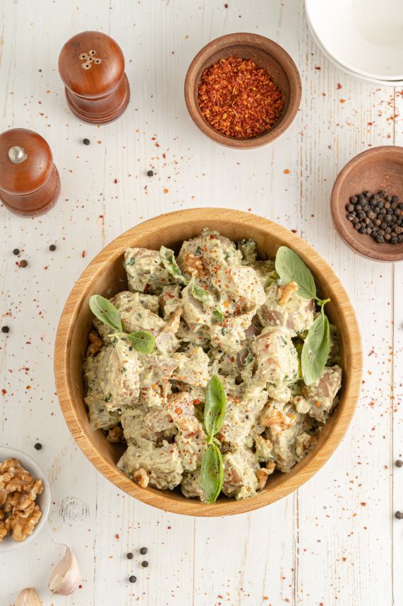 Overhead shot of pesto potato salad in a brown serving bowl with little bowls of spices and salt and pepper on the side