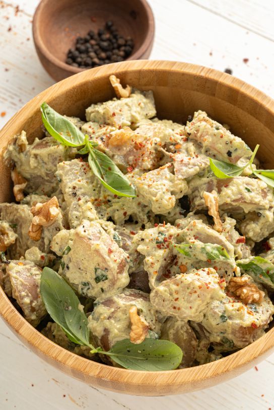 Up close shot of a wooden bowl containing potato salad with a creamy dressing and fresh basil