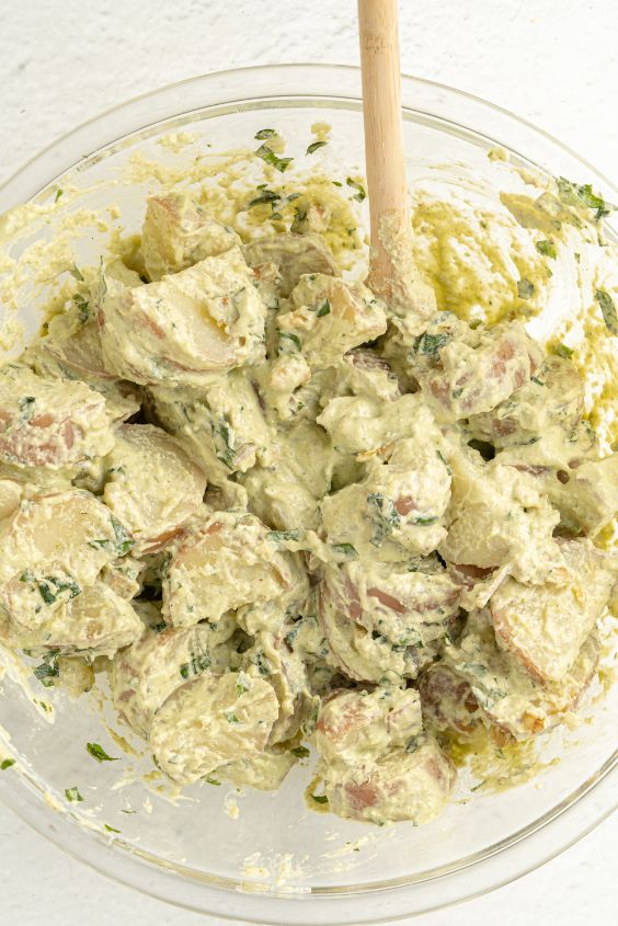 Potatoes and pesto salad dressing combined in a large glass bowl