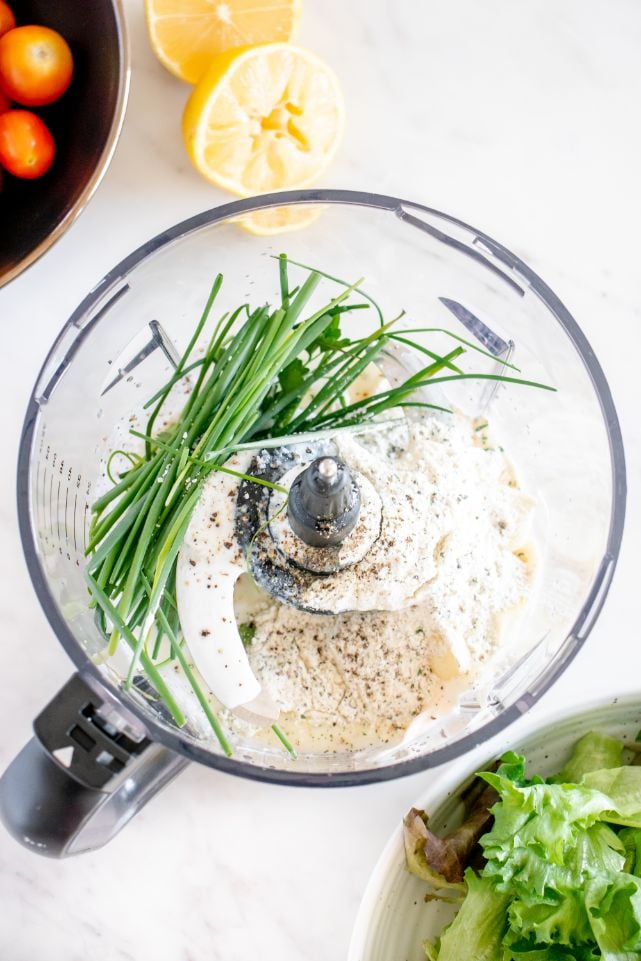 Ingredients for a herbed ranch dressing including fresh chives added to the bowl of a food processor