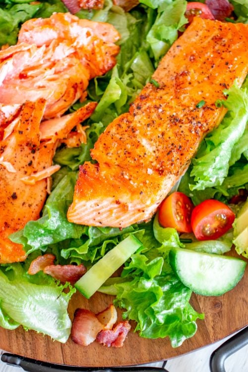 Up close shot of two cooked salmon fillets lying on top of a salad