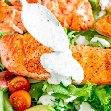Ranch dressing being drizzled over a spinach and salmon salad