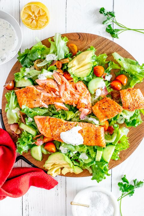 Salmon fillets with a BLAT salad and a creamy dressing on top of a large wooden chopping board