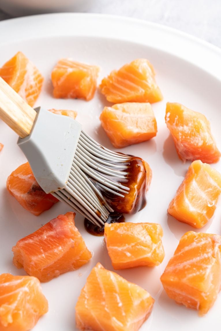 A silicone pastry brush brushing teriyaki sauce on to salmon chunks