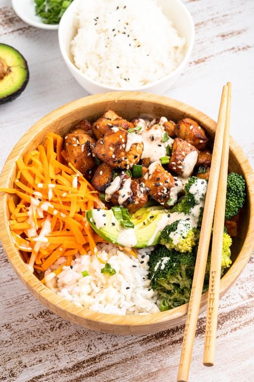 Salmon and broccoli with rice and avocado served in a wooden bowl with extra rice served on the side