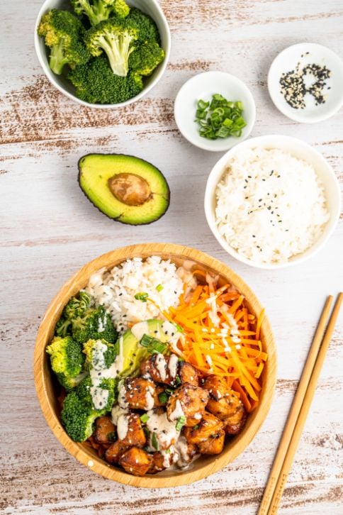 An overhead shot of a salmon sushi bowl with small bowls of condiments on the side