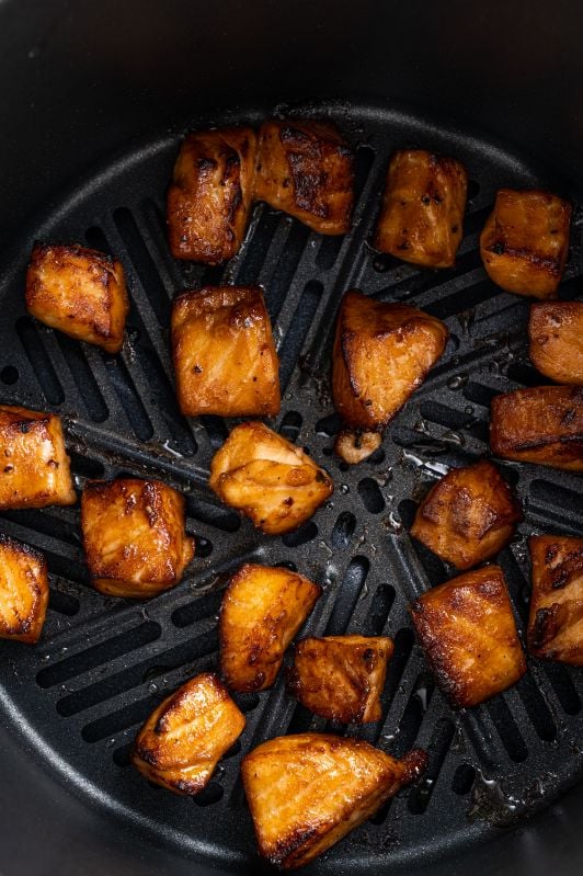 salmon chunks evenly distributed in the basket of an airfryer and cooked