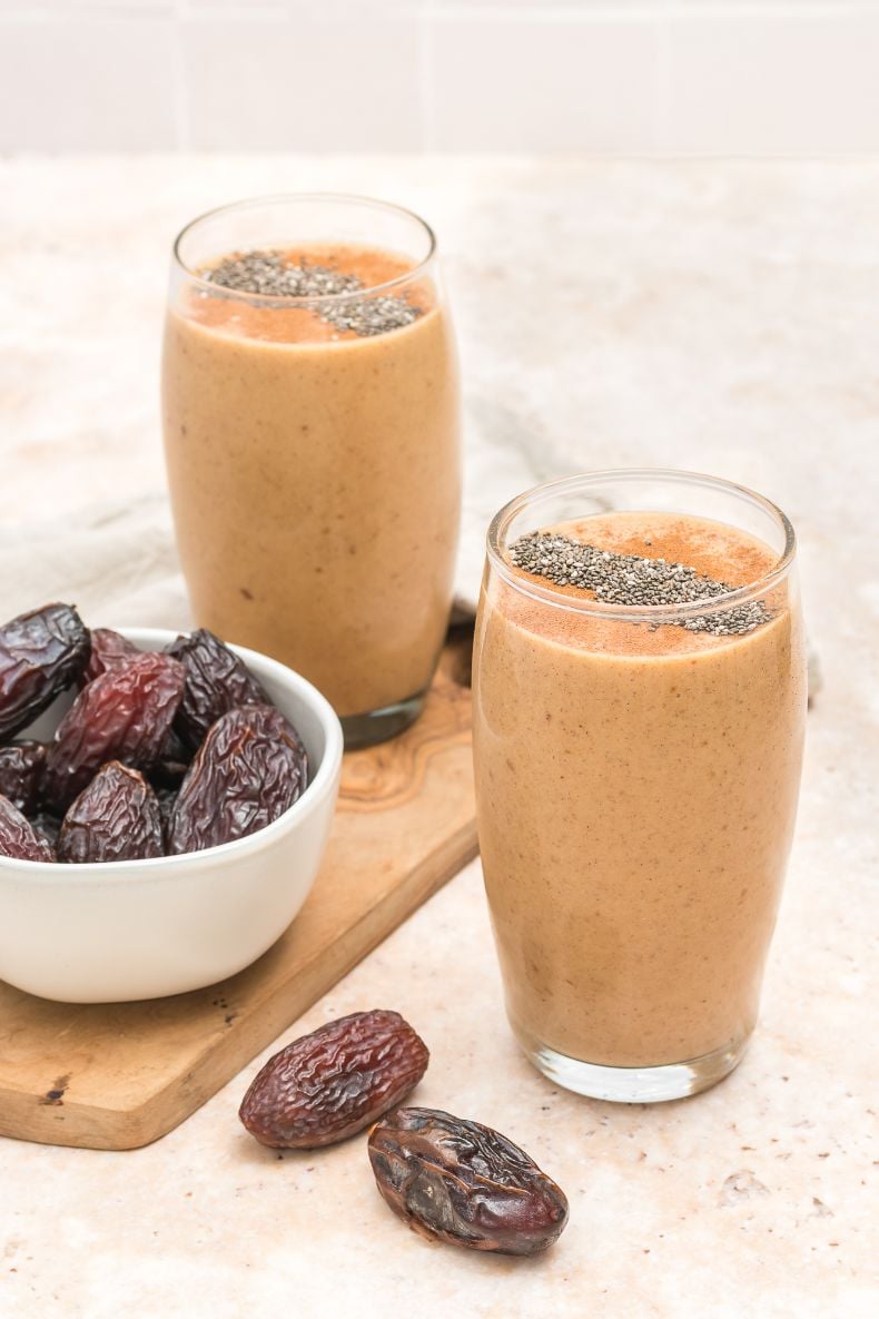 two banana and date smoothie served in tall glasses with fresh dates in a bowl beside them