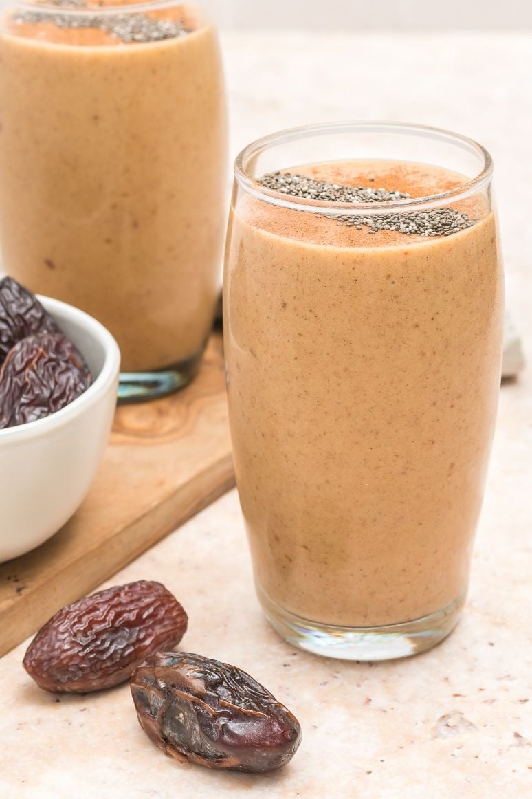 Peanut butter date smoothie served in a tall glass with some fresh dates surroounding it