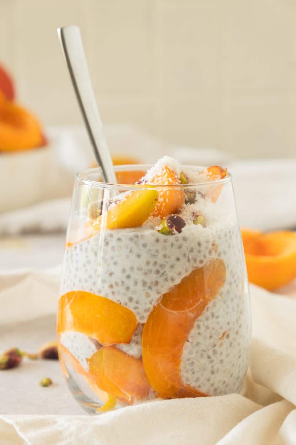 Chia pudding in a wine glass with slices of apricots around the side and a spoon poking out of the top
