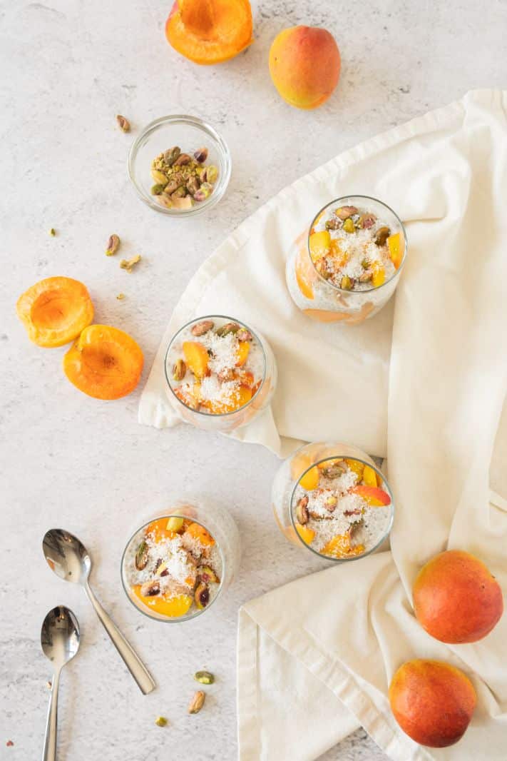 Overhead shot of 4 chia puddings served in glasses with fresh apricots surrounding them