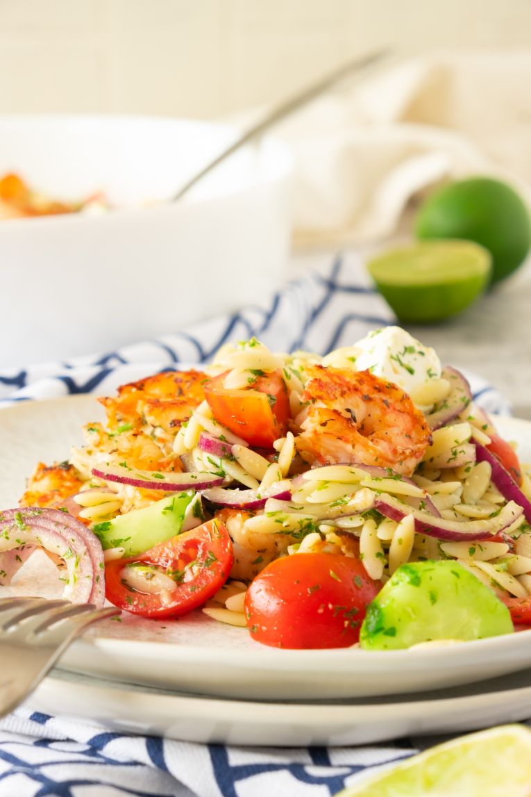 Mediterannean shrimp orzo pasta salad served on a white plate with some lime wedges in the background