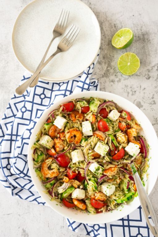 Cold pesto risoni and shrimp salad served in a large white bowl with some lime wedges