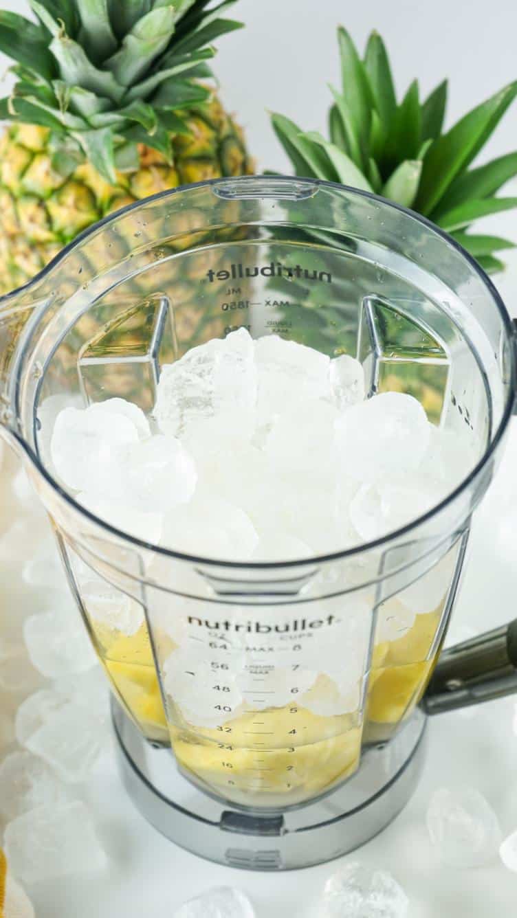 A blender full of pineapple, ice, water and sugar