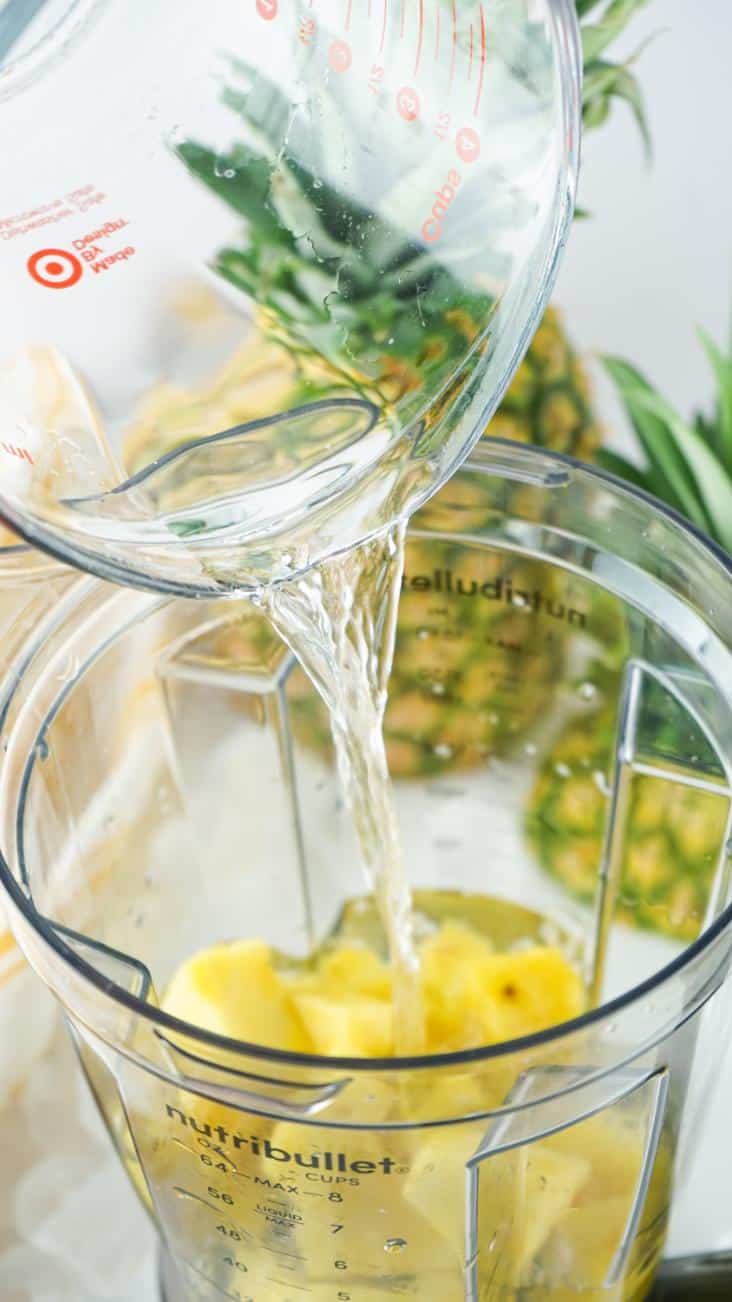 Water being poured into the jug of a blender that is full of pineapple