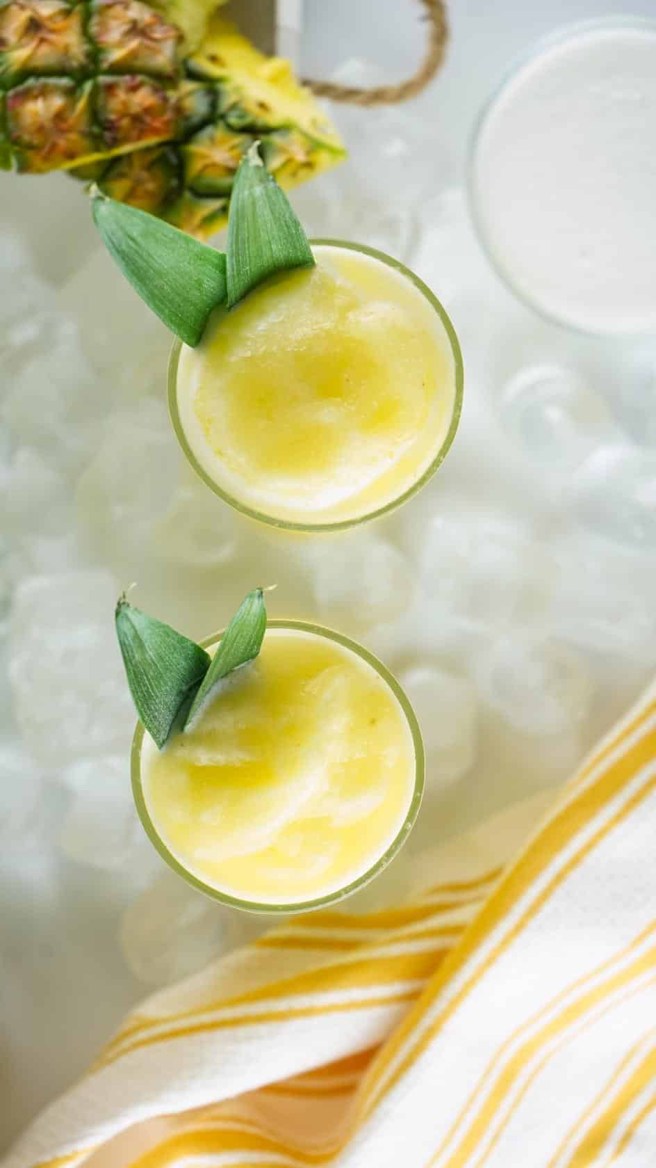 Overhead shot of a pineapple drink served in two glasses with pineapple leaves as a garnish