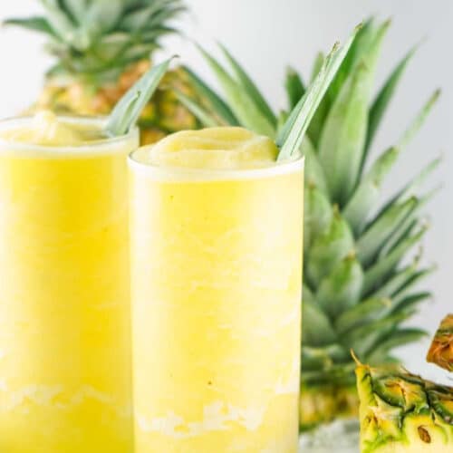 Iced pineapple agua fresca served in a glass with fresh pineapples in the background